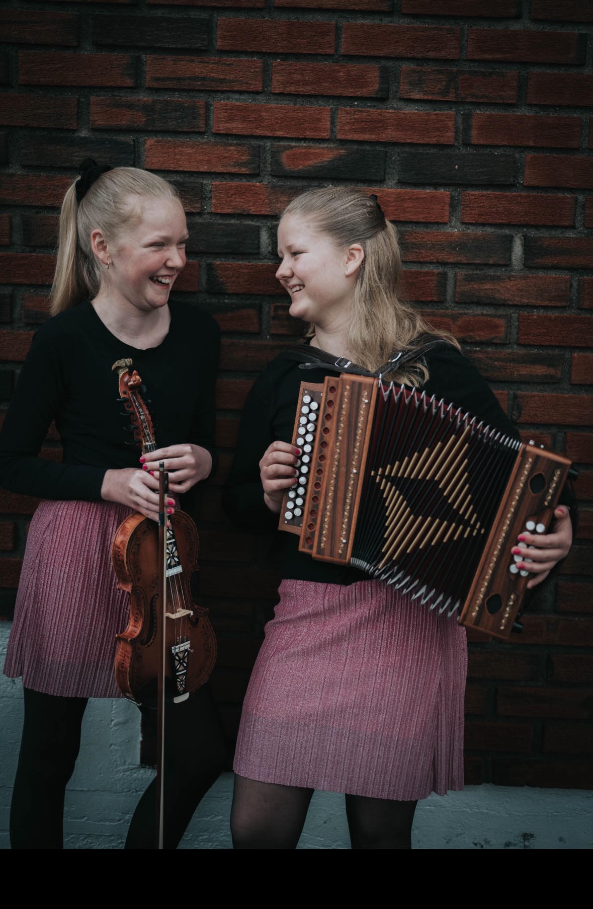 Silje og Anna Margrethe i make skjørt, og med kvart sitt instrument. Dei ler.